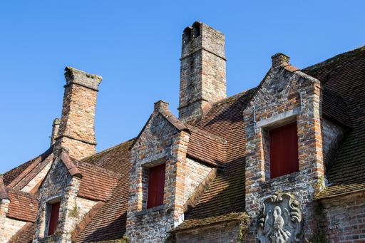 A low angle shot of old-style rooftops with chimneys under the blue sky in Bruges, Belgium