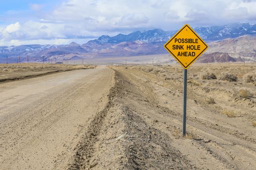 A traffic signs warns of "Possible Sink Hole Ahead" along a rural road.