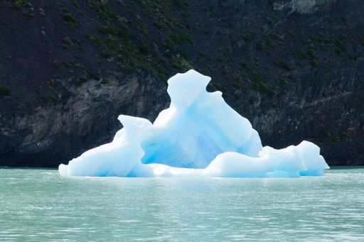 A striking iceberg floating in turquoise waters against a rocky backdrop in Patagonia, showcasing nature's beauty and serenity.