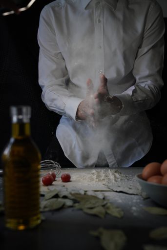 A person pouring flour from his hand onto the table to prepare food