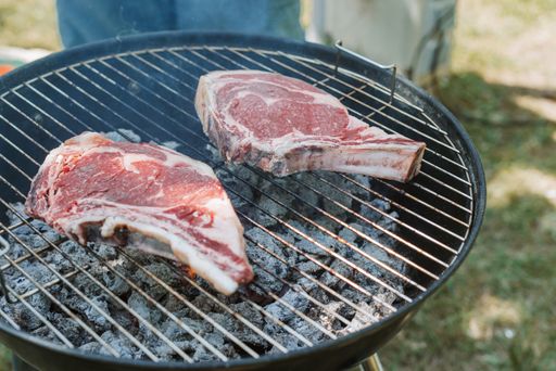 A closeup shot of two raw meat chops on the grill mesh with the field in the background