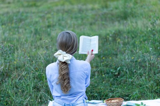 A back view of a blonde female with a beautiful trendy scrunchy on her hand reading a book
