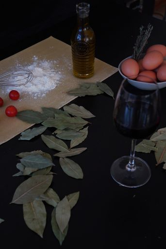 A glass of wine, leaves, syrup, tomatoes, flour and a bowl of eggs next to each other