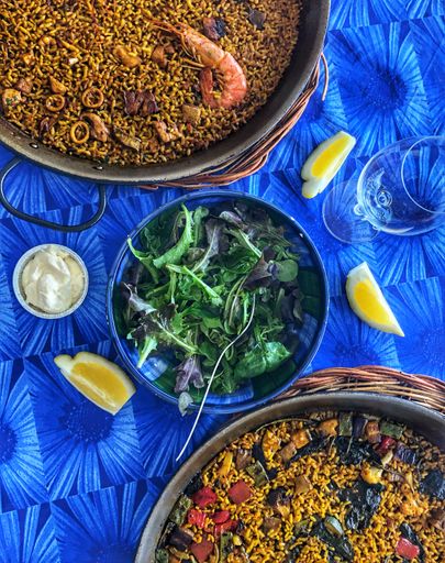 A vertical top view of Spanish food with sauce and sliced lemons on a blue table