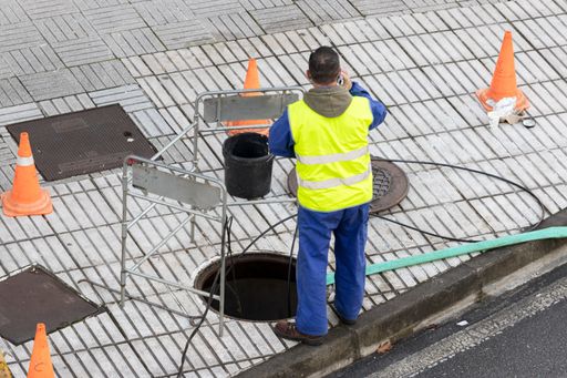 Telecommunications worker fixing wiring on urban sidewalk using smartphone