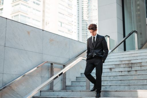 A serious young Caucasian guy dressed professionally walking down outdoor stairs
