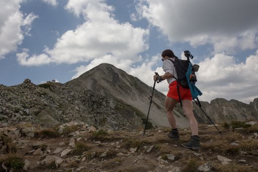 A low angle shot a hiker going up the rock-covered trail towards the mountain peak
