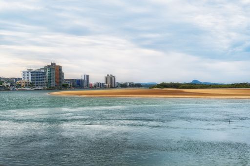 Scenic view of coastal city skyline with sandy beach and calm waters under a cloudy sky.