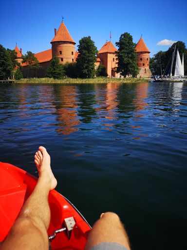 A vertical shot of  female leg on the shore with Trakai castle in the background on a sunny day