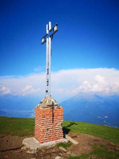 A vertical shot of a big metal cross on a brick platform on mountain top on a sunny day