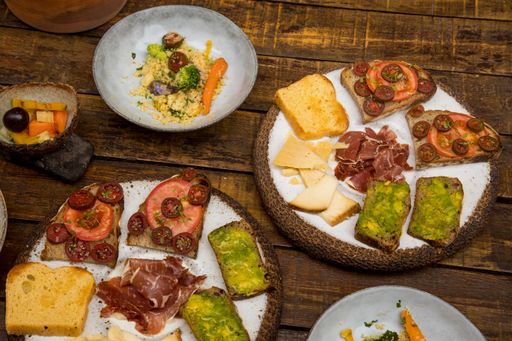 A top angle shot of servings of toasts with vegetables and plates with salads and fruits on a wooden table