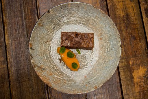 A top view shot of a silver plate with a chocolate pastry and a mango piece on a wooden table