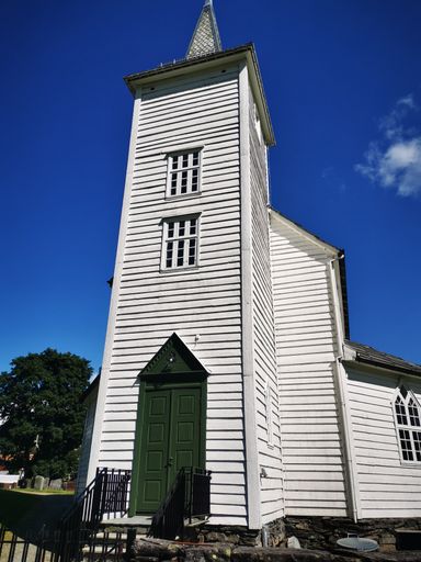 A vertical shot of a building with a sharp pyramid roof and a cross in the cemetery