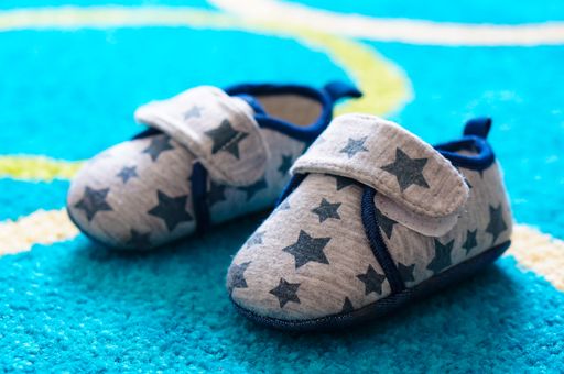 A close-up shot of a pair of small gray baby boy shoes with stars on a carpet floor