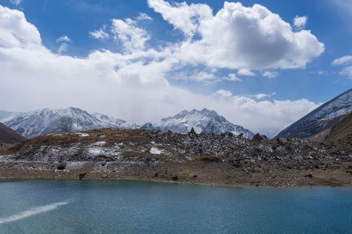 Scenic mountain landscape with snow-capped peaks under a cloudy blue sky, overlooking a tranquil turquoise lake.