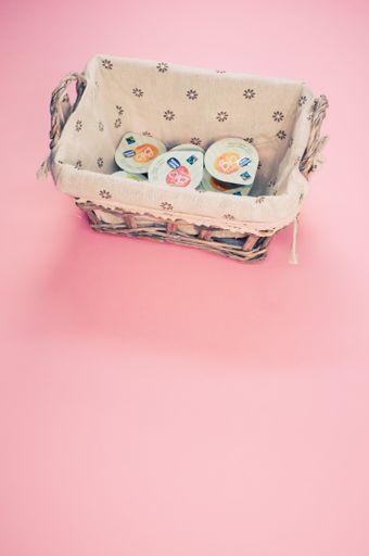A vertical shot of fruit jam on monodose packages in a wicker canister isolated on pink background