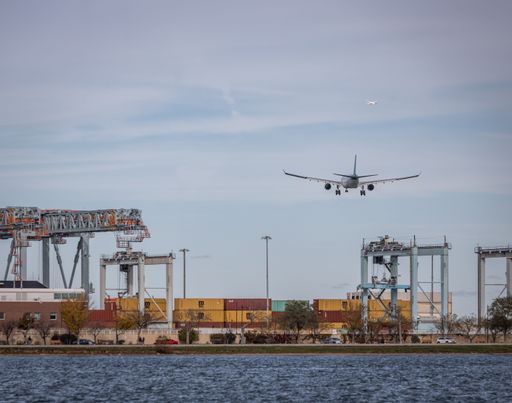 Airplane landing near a busy port with cranes and cargo containers