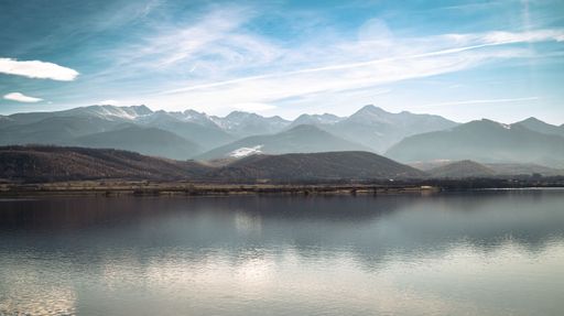 Peaceful mountain landscape with a serene lake reflecting the clear blue sky and distant peaks.