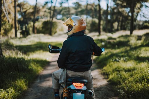 A person riding a motorcycle through a scenic forest trail, wearing a helmet and jacket, enjoying the outdoor adventure.