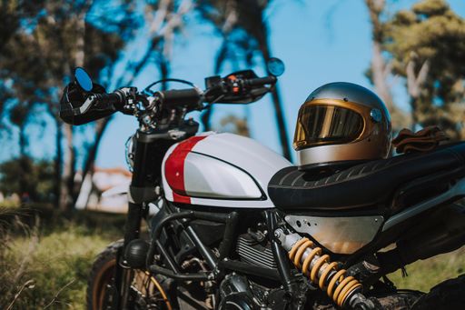 Close-up of a motorcycle with a vintage helmet on the seat, set in a scenic outdoor location with trees in the background.