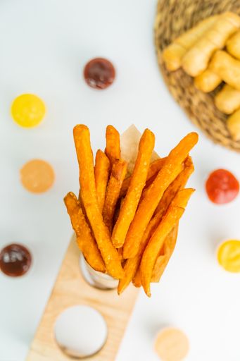 Top view vertical photo of fried sweet potatoes in a cone with dip sauce and tequenos in the background out of focus.