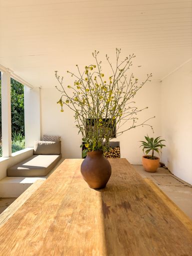 Wild flowers in a vase on a wooden table on a sunny veranda in a vintage farmhouse decor style.