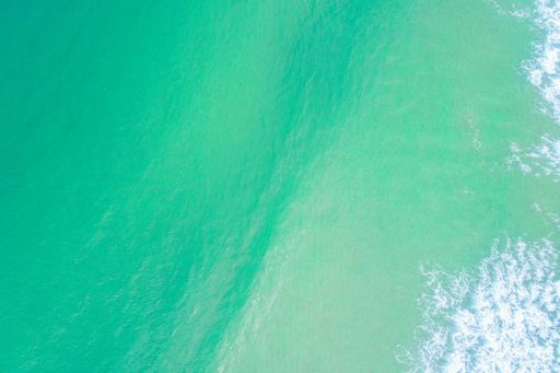An aerial view of a beautiful turquoise ocean. The water is crystal clear and the waves gently crash against the shore.