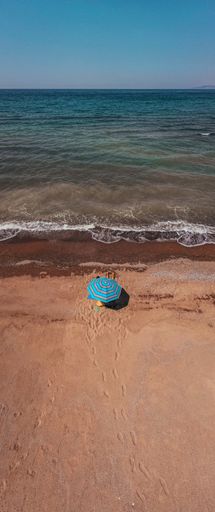 A vertical shot of a seashore at daylight with one blue umbrella