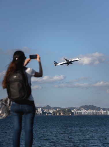 A vertical closeup of a girl taking a picture of a flying plane.