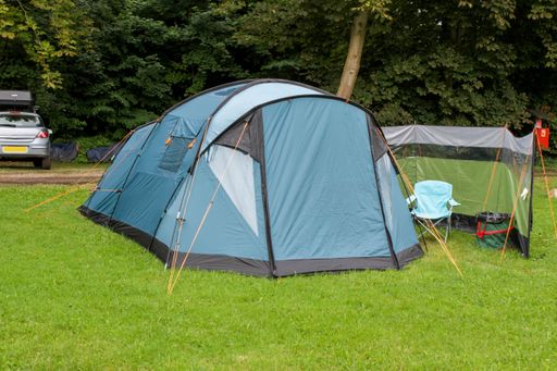 A close-up shot of a blue tent on the grass surrounded by trees