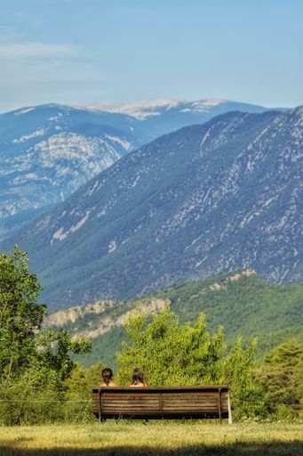A vertical shot of two people sitting on a bench in nature and enjoying the view of the mountains