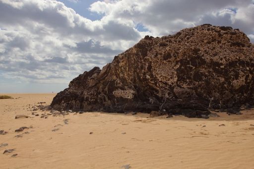 A big dark brown rock in the sandy beach under the bright sky