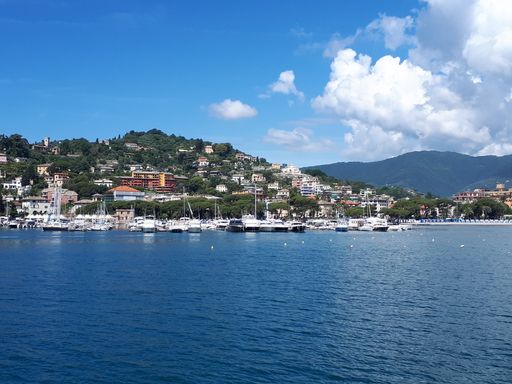 A high angle shot of a bay with small ships in blue waters and urban setting on the seashore