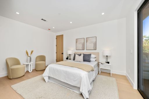 Modern minimalist bedroom interior with neutral tones, featuring a cozy bed, elegant decor, and natural lighting from a large window.