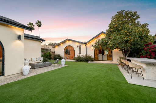 Modern backyard with lush lawn, seating area, and outdoor bar at sunset in a suburban setting.