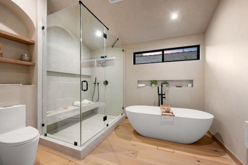Modern bathroom with glass shower, freestanding tub, and wooden floor, featuring minimalist design and natural lighting.