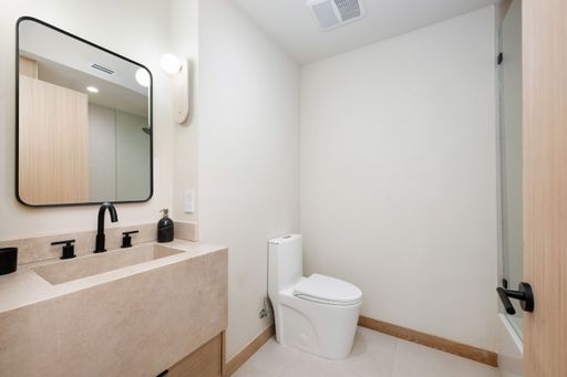 Modern minimalist bathroom interior with beige tones, featuring a sleek vanity, black fixtures, and a toilet.