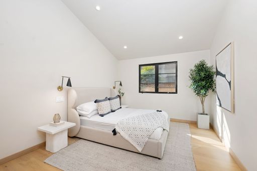 Modern minimalist bedroom with neutral tones, featuring a cozy bed, stylish decor, and natural light from a window.
