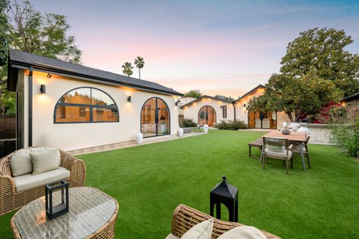 Modern backyard with lush green lawn, wicker furniture, and elegant lighting at sunset.