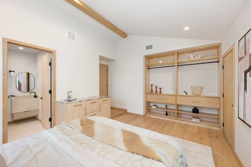 Modern bedroom interior with wooden accents, open closet, and ensuite bathroom featuring minimalist decor.