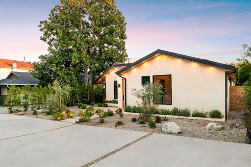 Modern suburban house with landscaped front yard at sunset, featuring clean lines and warm lighting.