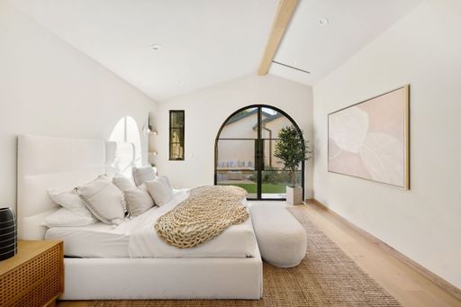 Modern minimalist bedroom with natural light, featuring a cozy bed, large window, and elegant decor in a neutral palette.