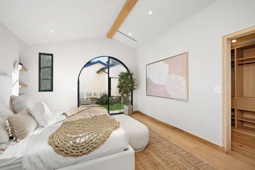 Modern bedroom with natural light, cozy decor, and open wardrobe, featuring large windows and wooden flooring.