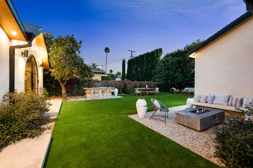Modern backyard with lush greenery, fire pit, and outdoor seating in a serene residential setting at dusk.