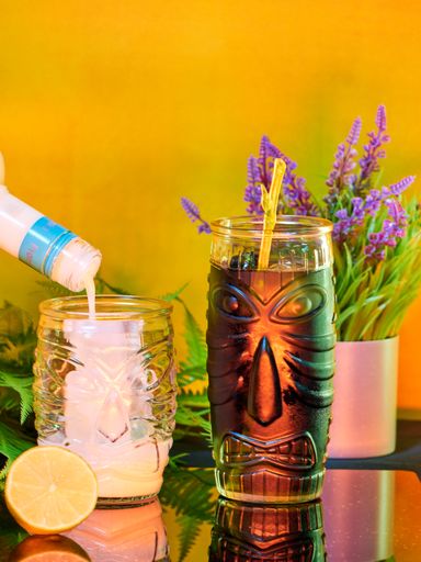 A vertical shot of drink pouring into a glass with tiki face