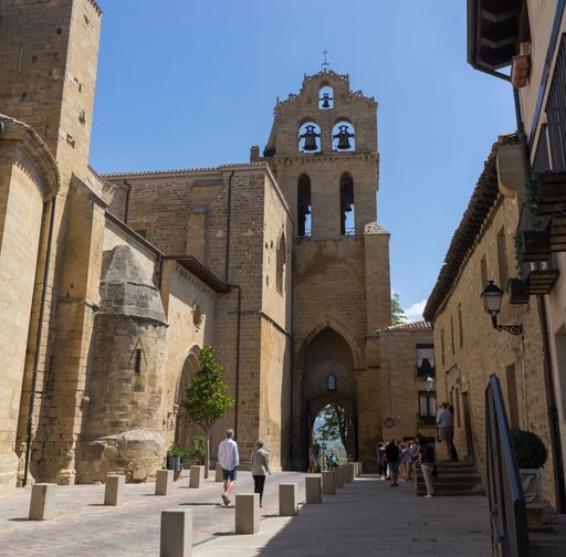 Medieval streets in the town of LaGuardia where several tourists stroll and in the background the Puerta de San Juan and bell tower of the Church.