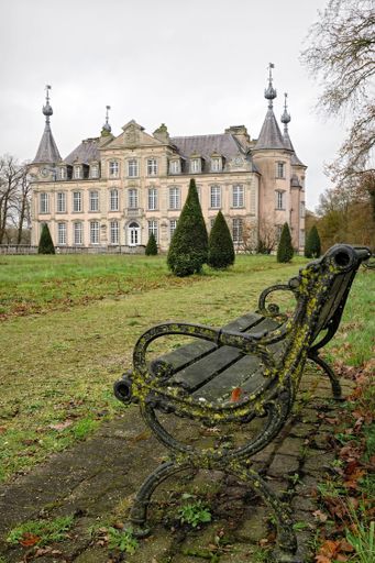 Poeke Flanders Belgium  A moss-covered bench in front of a historic European castle with pointed towers, surrounded by a grassy area and trees.