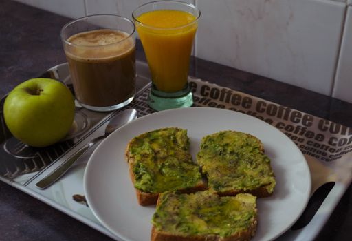 A breakfast with avocado on toast with a green apple, coffee, and juice