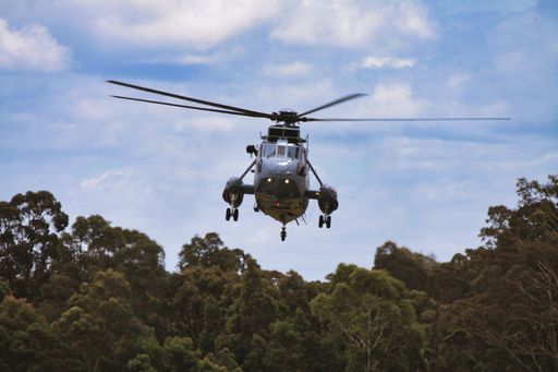 a closeup of a blue helicopter flying in the air on cloudy sky background above the forest