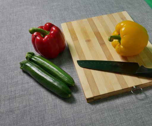 A high angle shot of bell pepper and cucumber on a wooden board with a knife on kitchen table